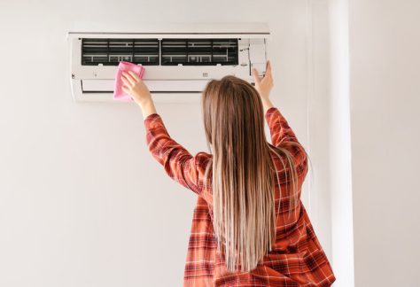 Young woman cleaning air conditioner at home